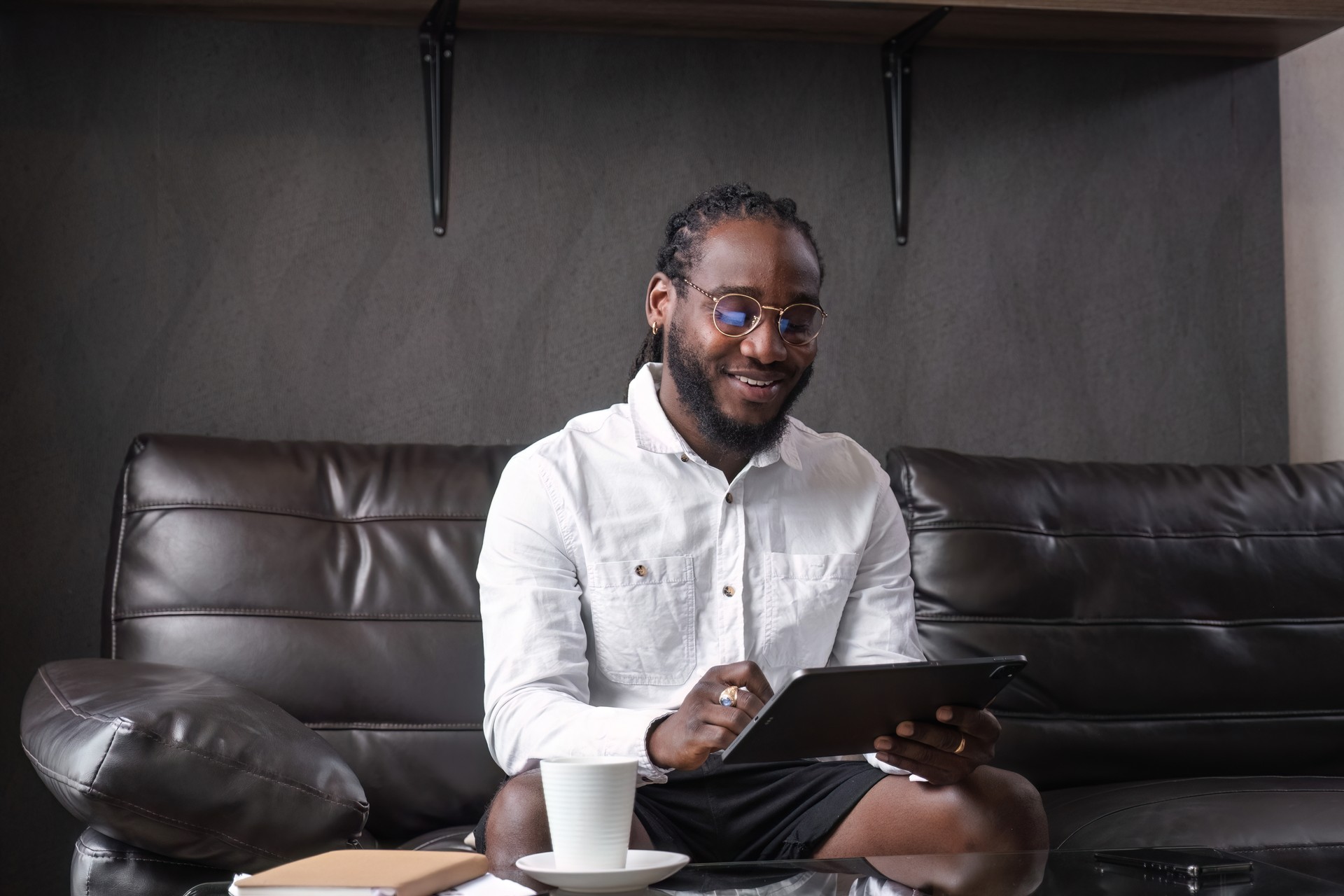 Jeune homme afro-américain travaillant en ligne depuis chez lui sur une tablette dans un salon moderne