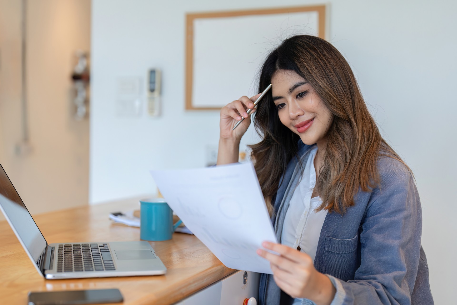 Jeune femme freelance travaillant à domicile avec un ordinateur portable et des documents dans un cadre de bureau à domicile moderne